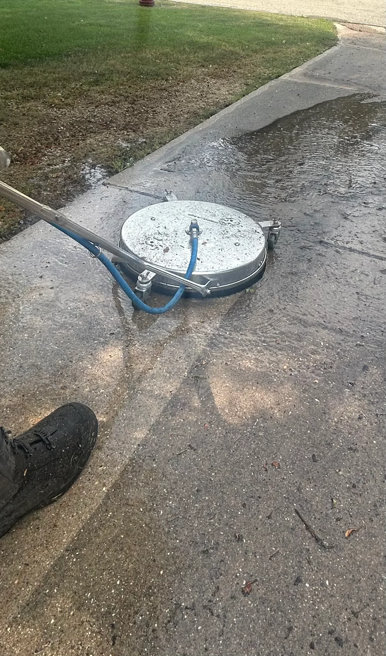 A Madison, WI residential concrete driveway after professional pressure washing, showing clean gray surface free of algae streaks, oil stains, and salt residue. The cleaned driveway contrasts with a still-dirty section near the garage apron, illustrating the results of exterior driveway cleaning service.